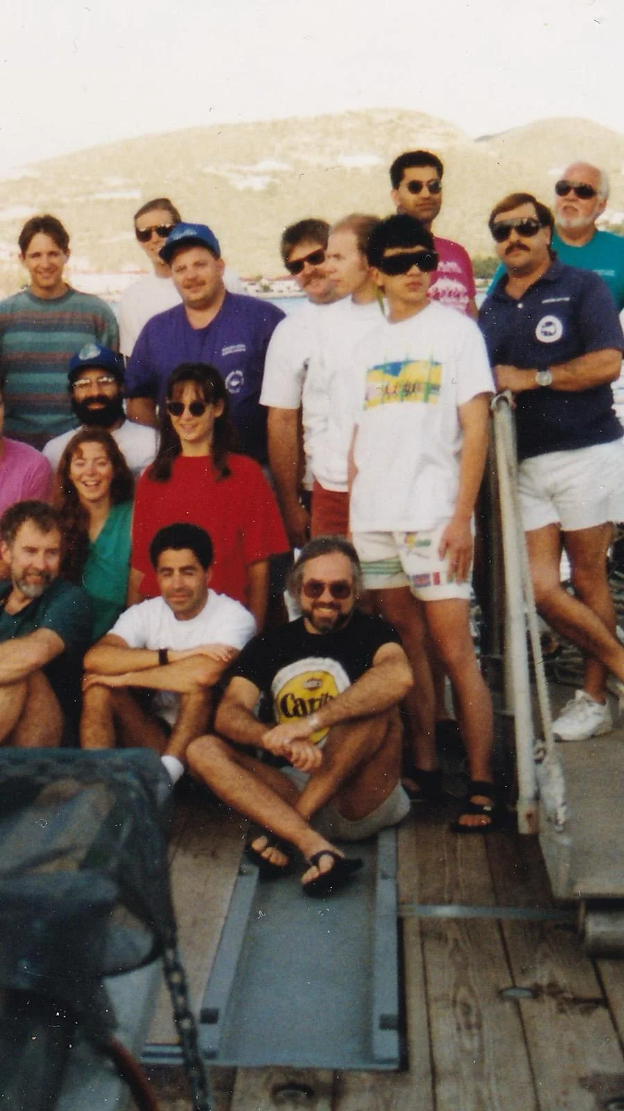 An old photo of a large group standing on the deck of a boat. In the center, Jon Zehr is sitting on the ground.