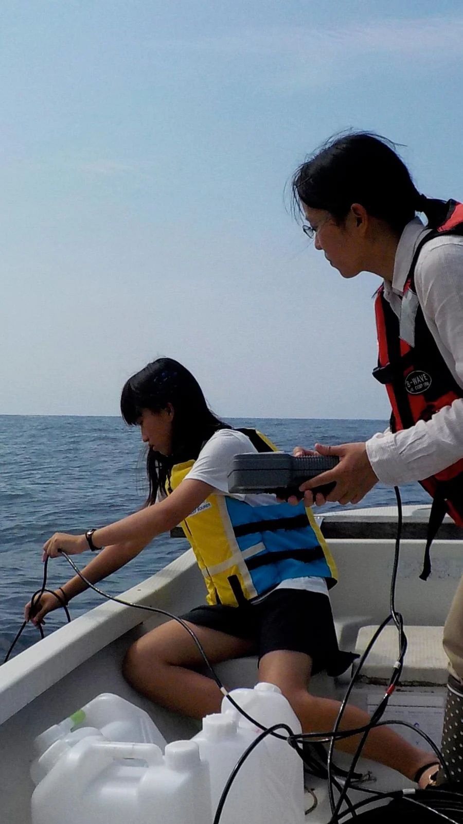 An adult woman and a child collect seawater off the side of a boat