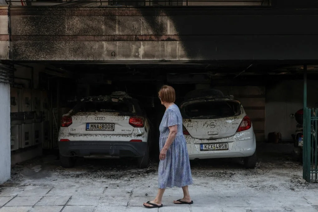 A woman walks past damaged cars and a building after attackers firebombed three residential buildings linked to Greece’s governing party in the northern city of Thessaloniki, Greece on July 1. Photo: Reuters