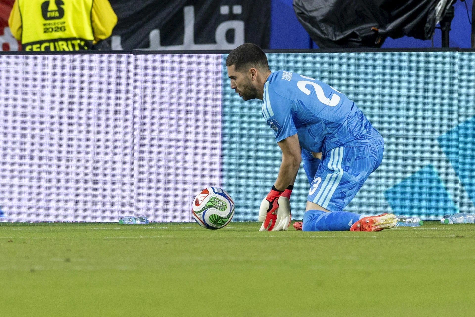 A goalkeeper in blue parries a ball.