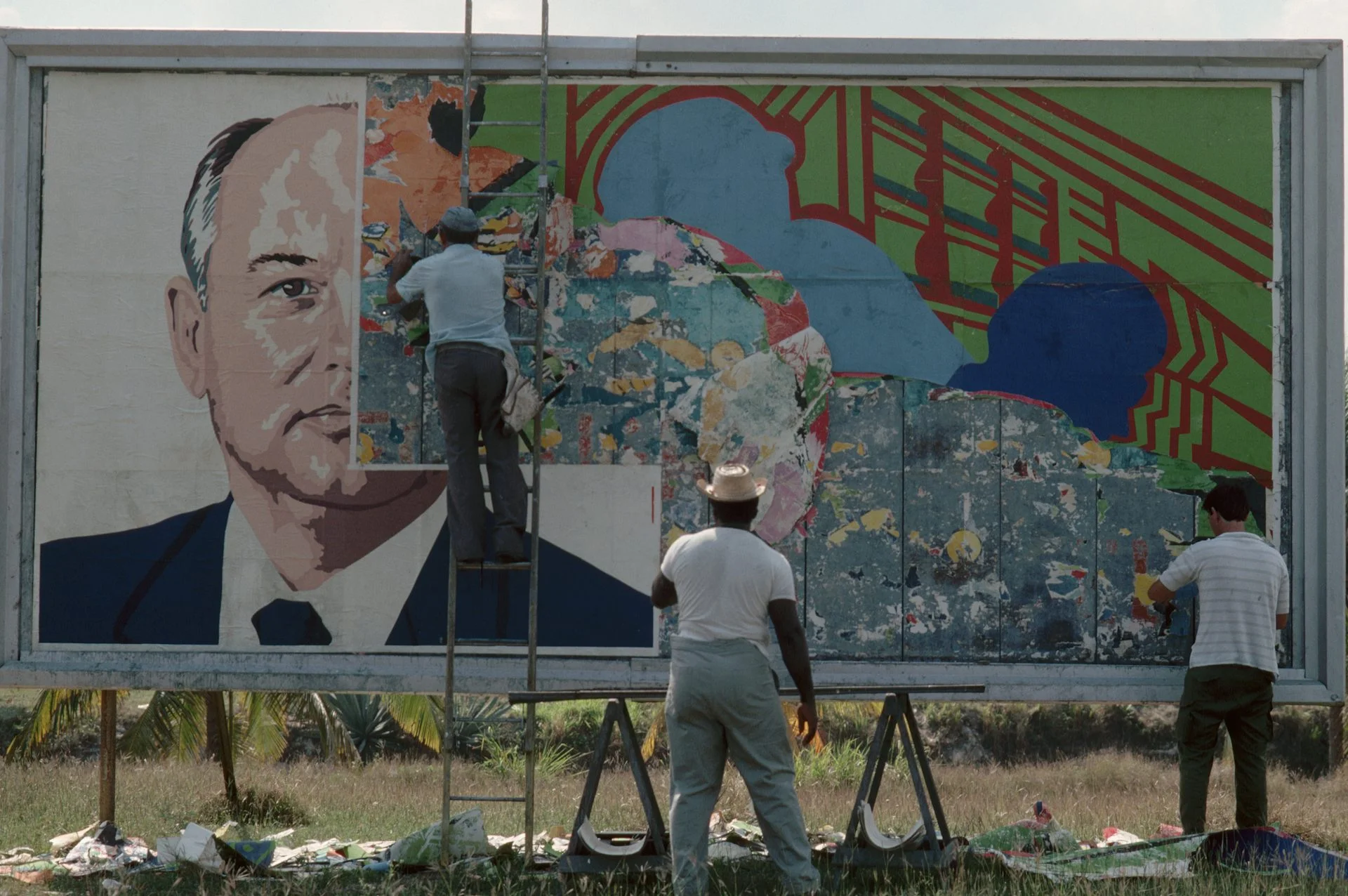 Two men paste over the image of a man on a billboard