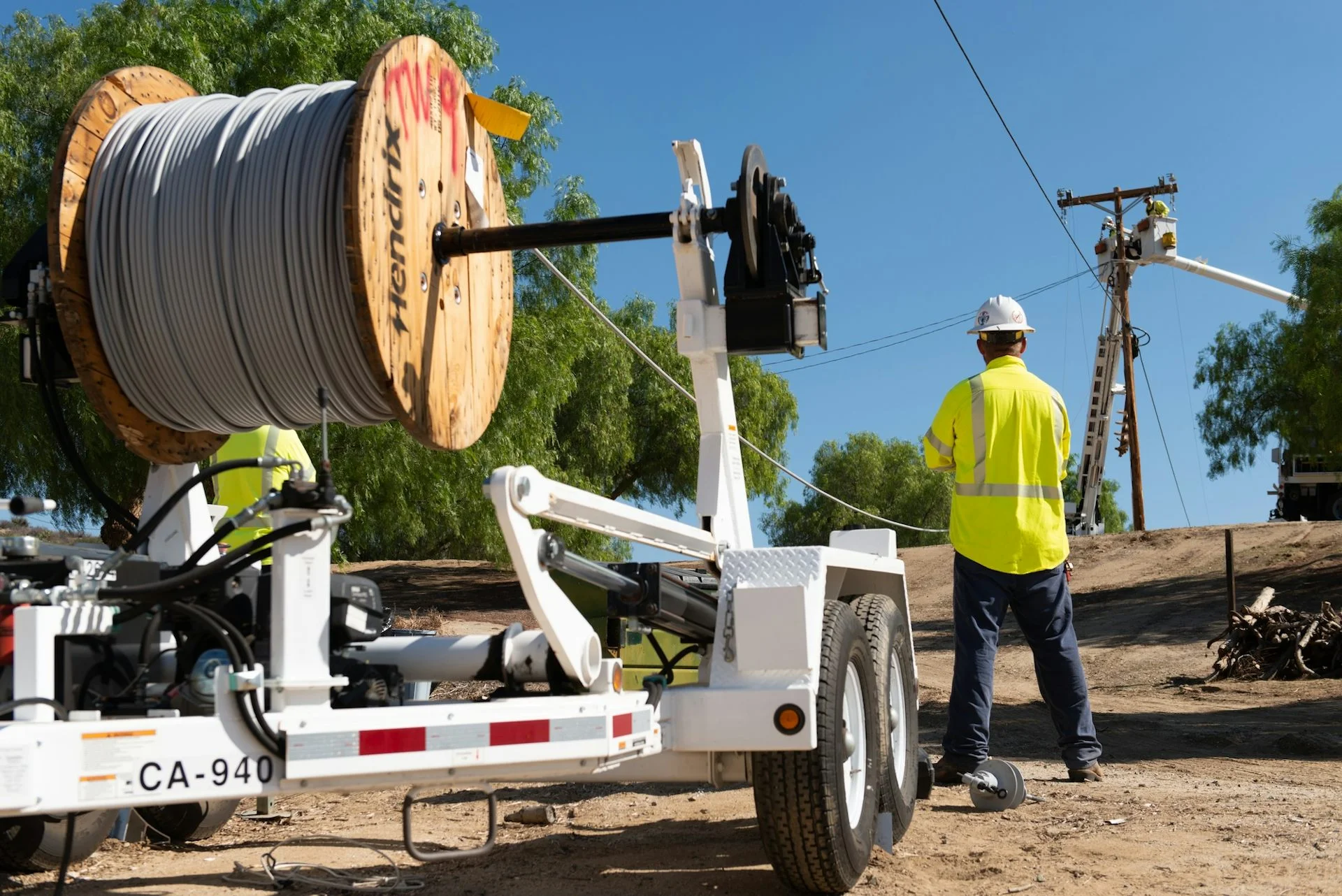 A worker stands by a giant roll of covered conductor line – power lines covered in a plastic.