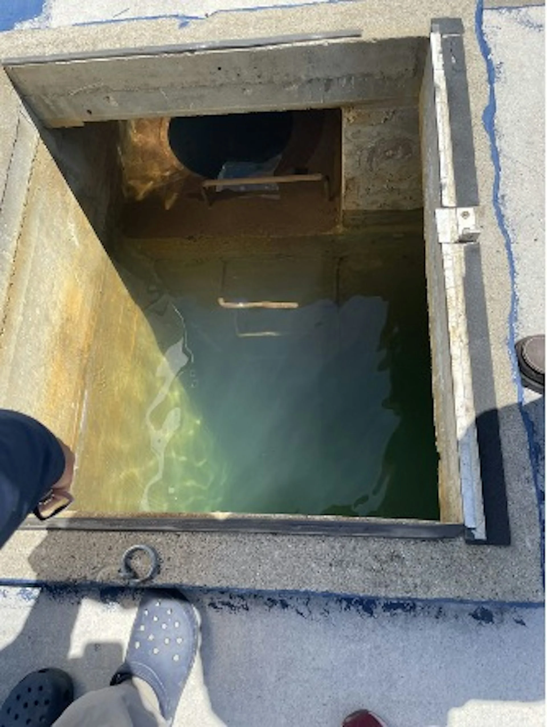 An open box in the ground with water inside.