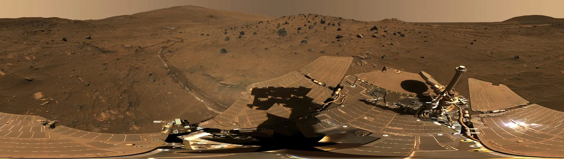 A panoramic view of a rocky, barren landscape with metallic equipment in the foreground.