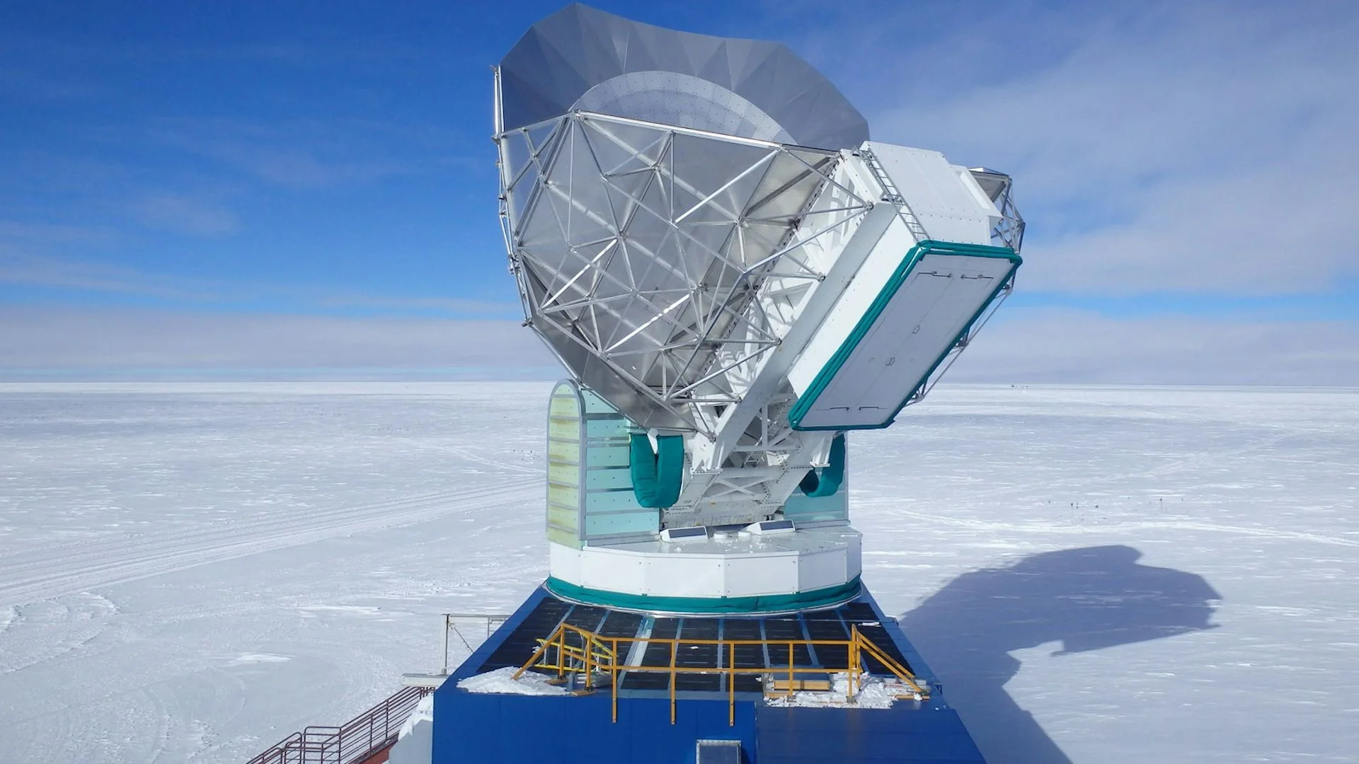 A large mechanical device sits atop a sheet of ice that stretches to the horizon.
