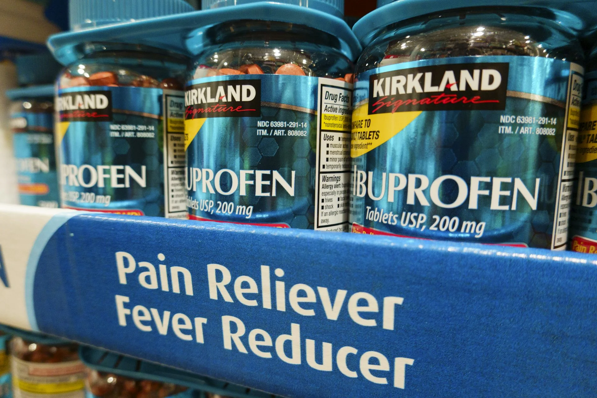 A shelf displaying bottles of ibuprofen, which are clear and full of small, circular pills